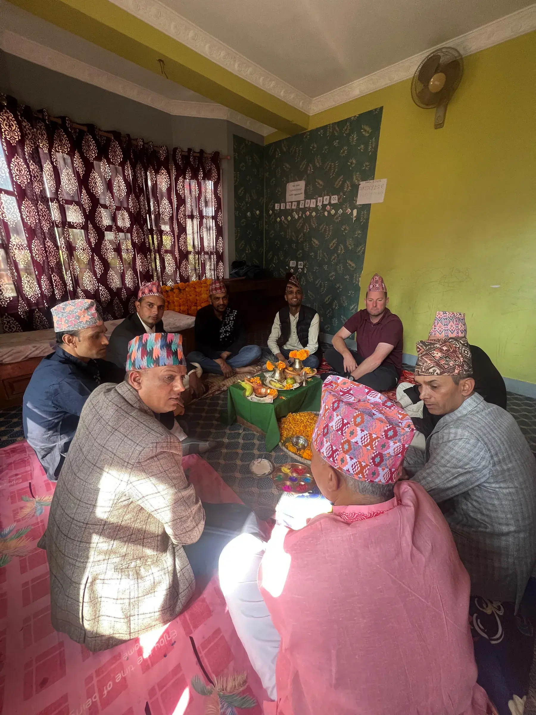 Joe sitting with the Nepali team around an offering of marigolds during a ceremony